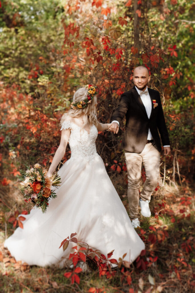 Bride and groom walking through an autumn forest, embracing fall wedding trends with earthy tones and natural outdoor settings in 2024.